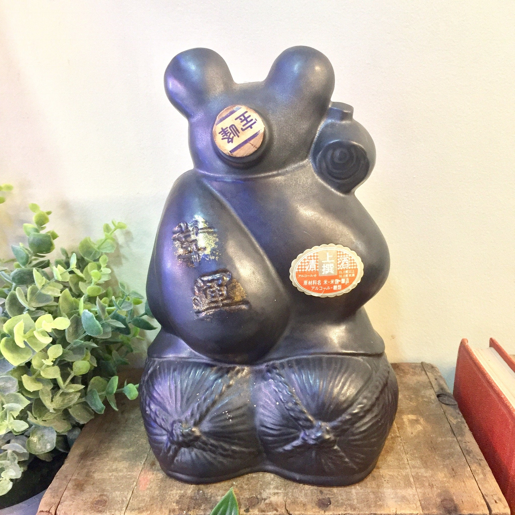 Vintage black and gold ceramic rat-shaped sake bottle with unique embossed designs, displayed on wooden surface with plants, an interesting and rare piece of Asian home decor.