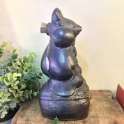 Vintage black and gold ceramic sake bottle shaped like a seated rat or mouse figure on a wooden surface with greenery in the background.
