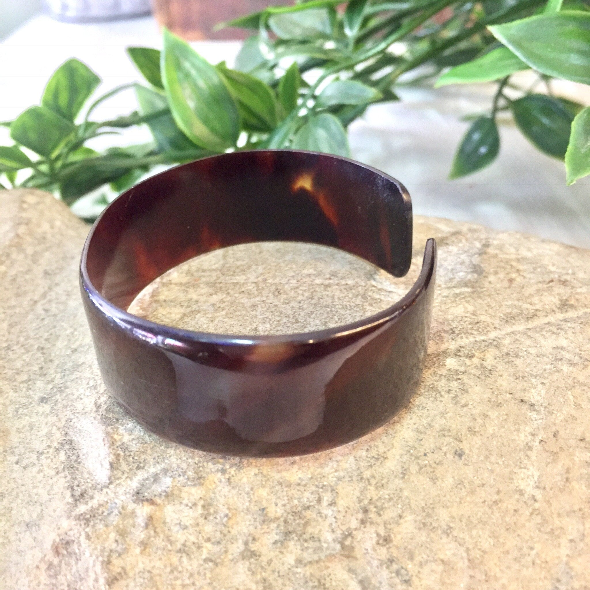 Vintage brown tortoise shell pattern plastic cuff bracelet on textured surface with plant leaves in background