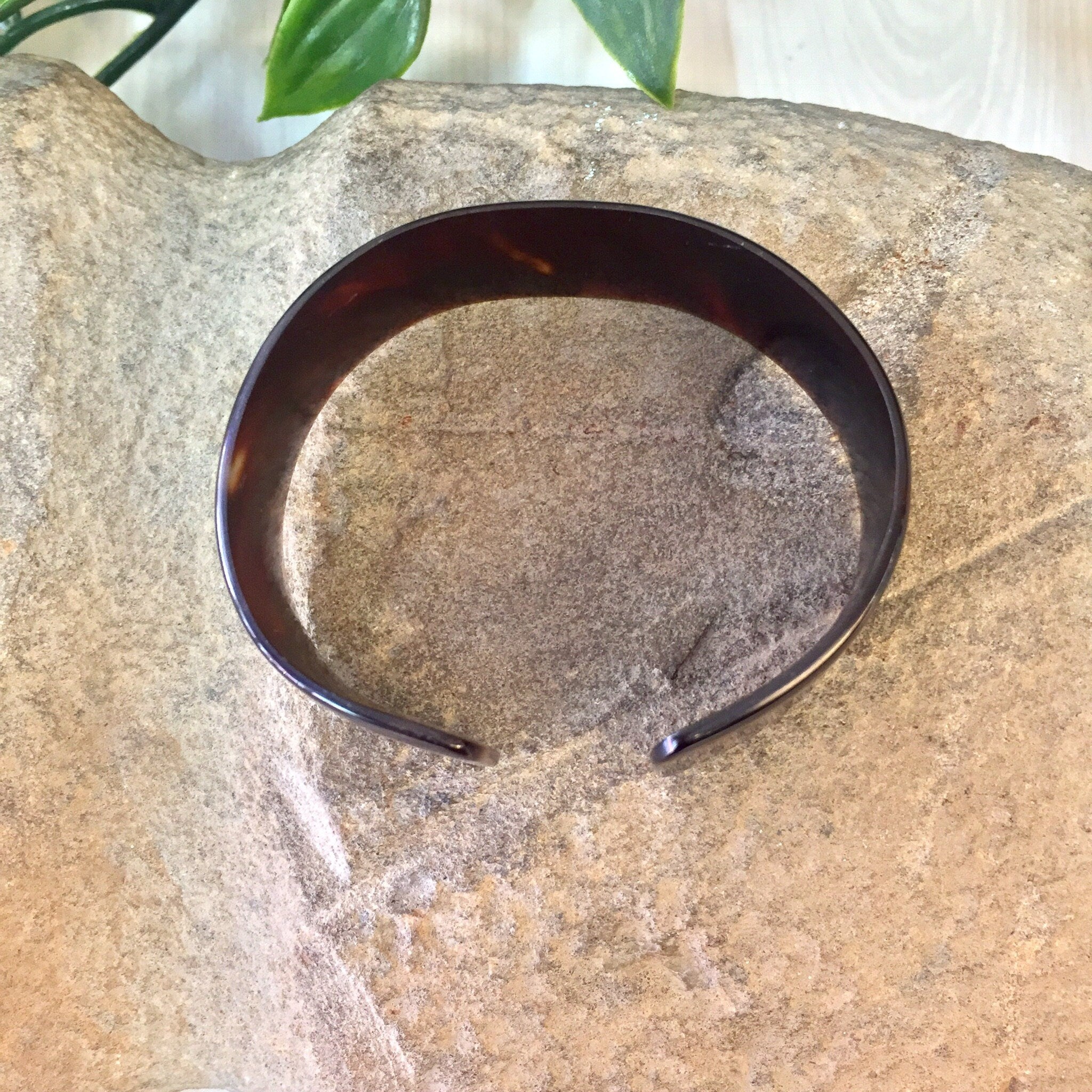 Vintage brown tortoise shell plastic cuff bracelet placed on stone surface with plant leaves in background