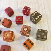 Antique wooden dice in various colors including red, brown and green with gold-colored pips scattered on a white wooden surface
