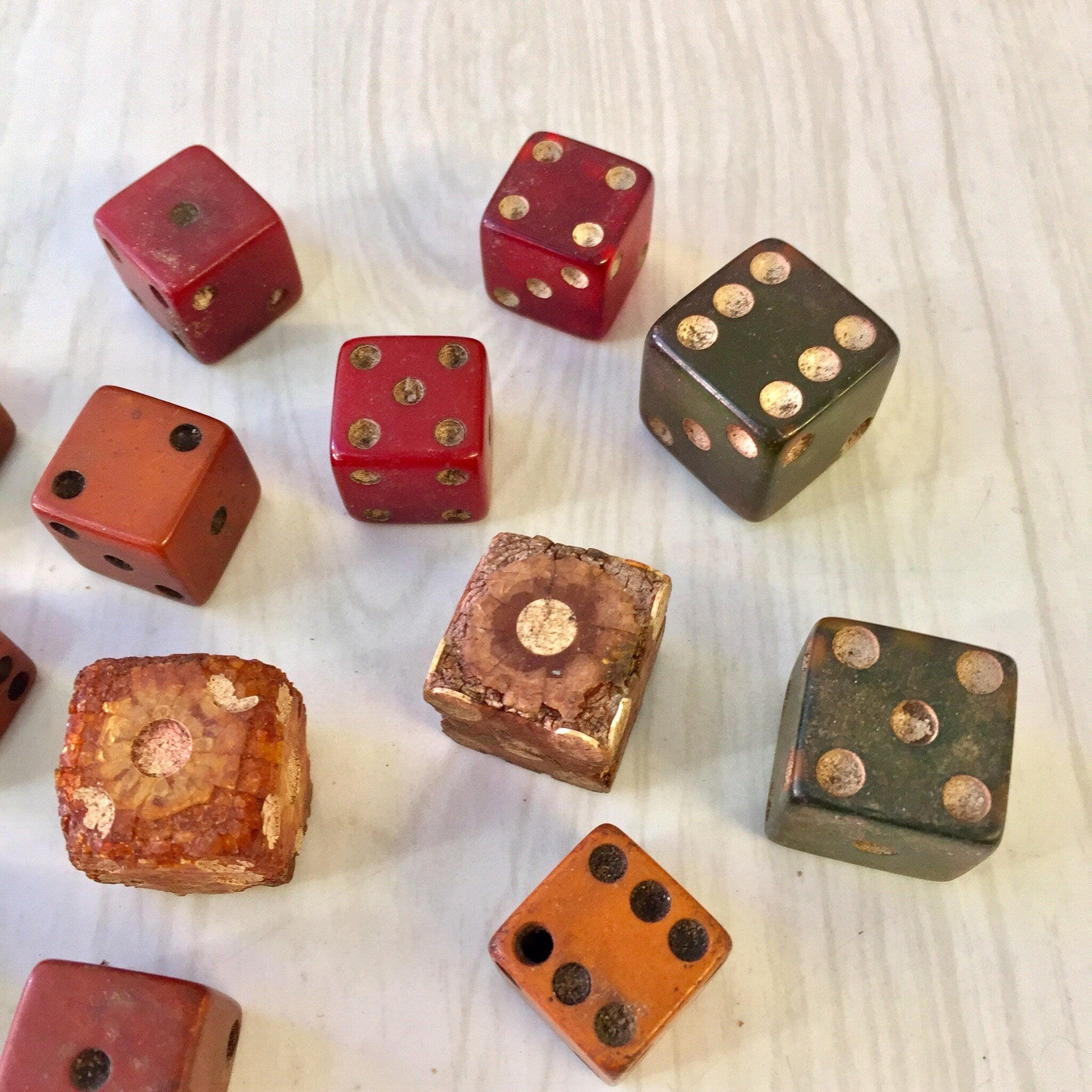 Antique wooden dice in various colors including red, brown and green with gold-colored pips scattered on a white wooden surface