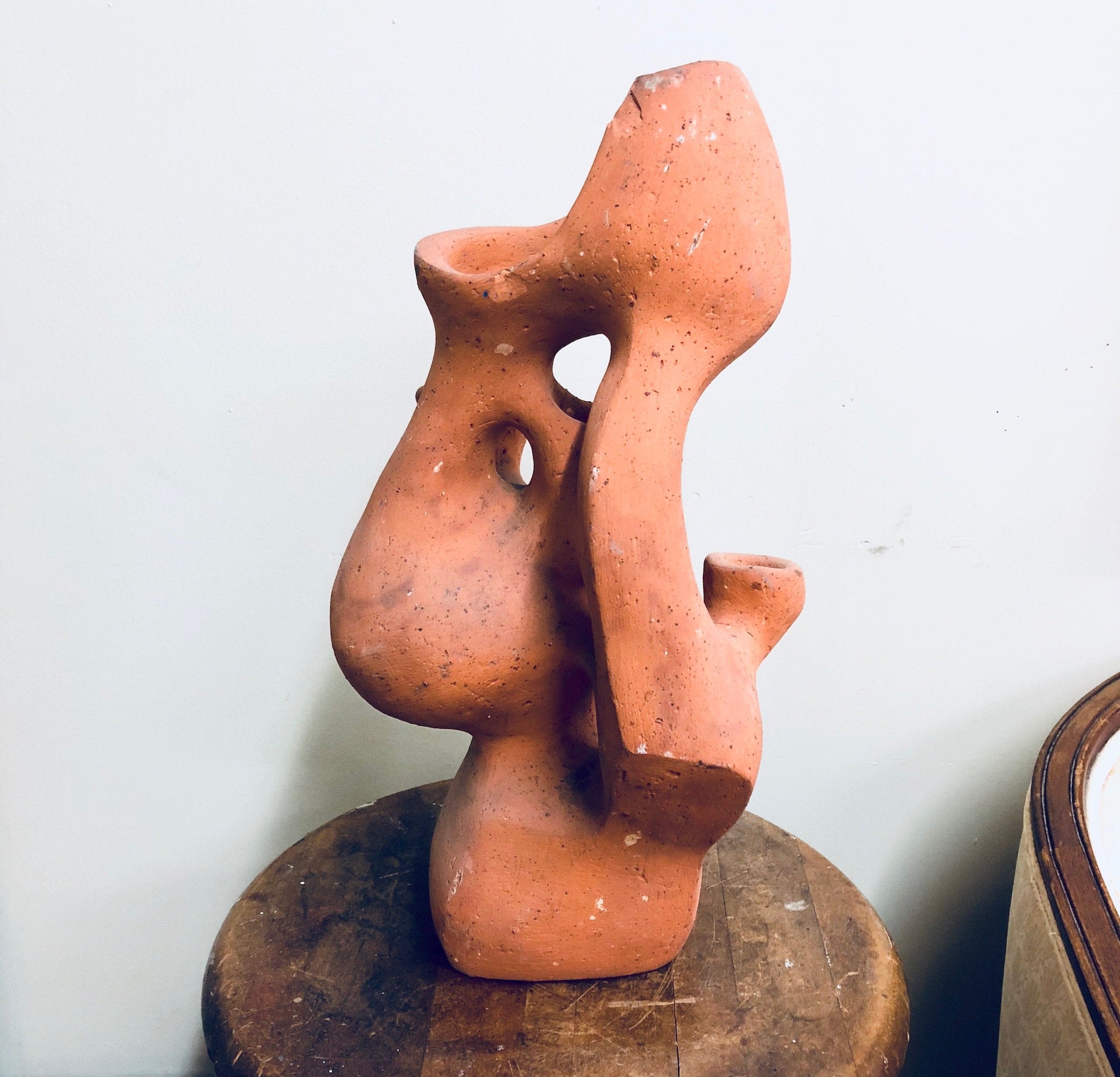 Terracotta sculptural planter in the shape of an abstract human face with holes for plants, displayed on a wooden surface against a white background.