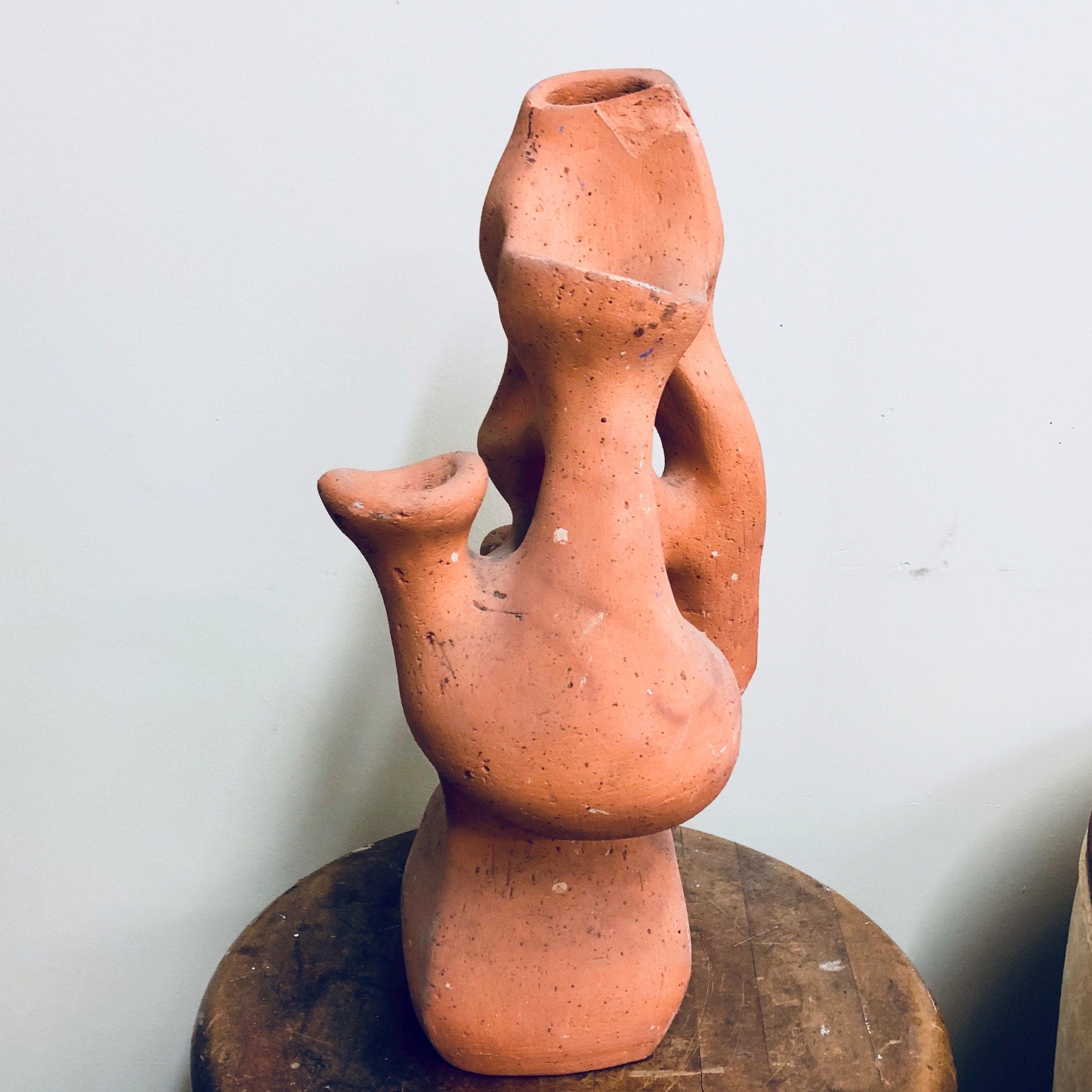Terracotta clay planter shaped like an abstract human figure with openings for growing strawberry plants or herbs. The rustic ceramic sculpture has an organic, handmade appearance.