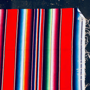 Colorful vintage Mexican blanket with red, blue, green, pink and white stripes, featuring tasseled fringes, suitable for use as a throw or picnic blanket.