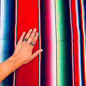 Hand touching colorful striped Mexican blanket with red background and blue, green, pink, and white stripes and fringe tassels
