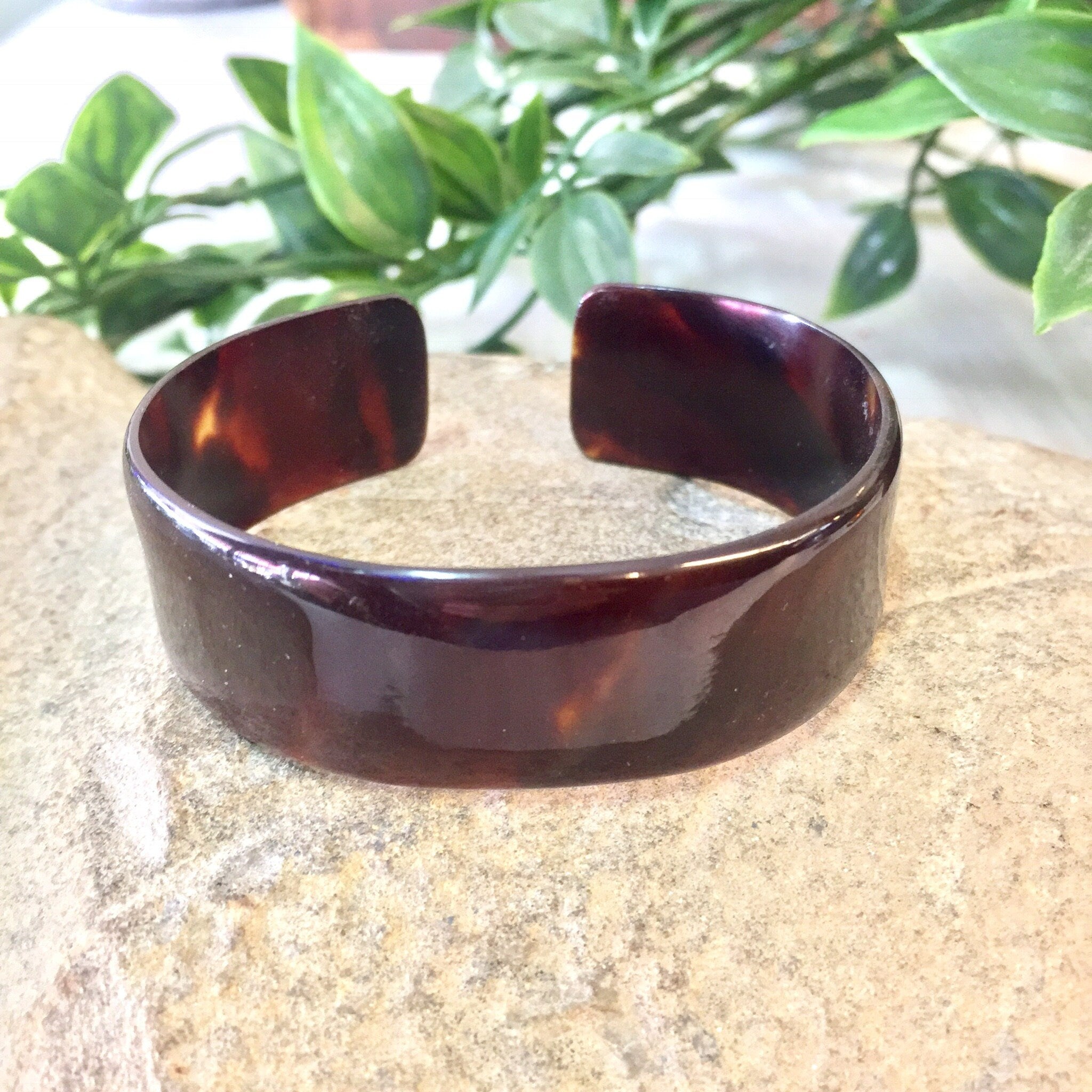 Vintage brown tortoise shell plastic cuff bracelet on stone surface with greenery in background