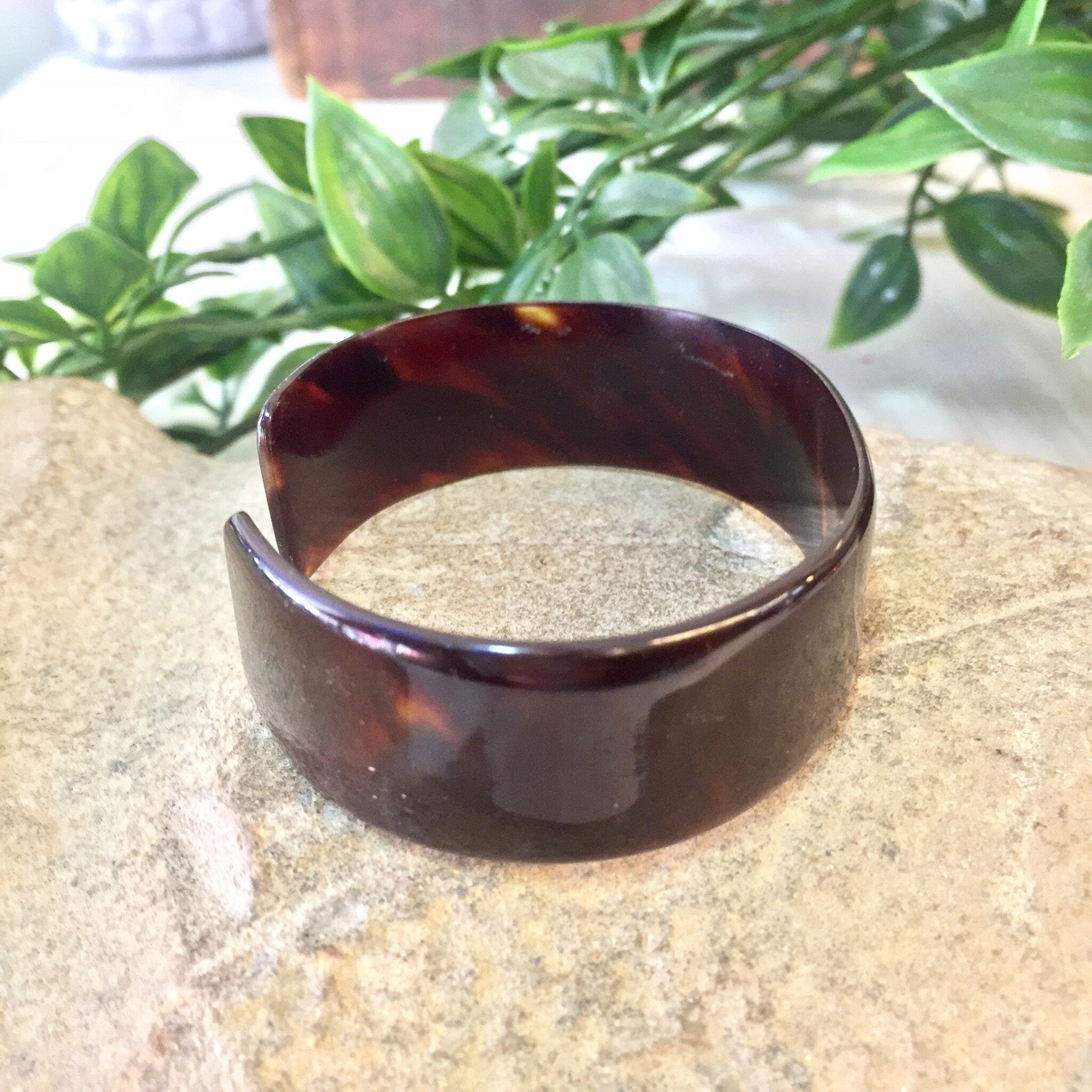 Vintage brown tortoise shell plastic cuff bracelet displayed on stone surface with greenery in background