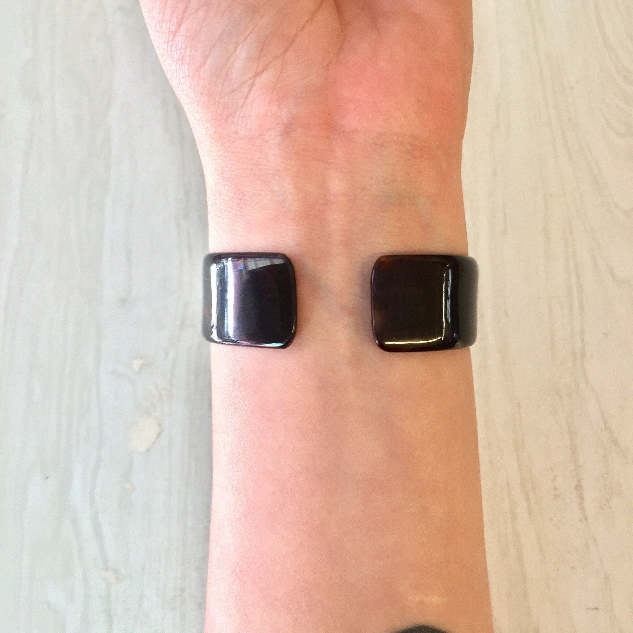 Vintage brown tortoise shell plastic cuff bracelet on person's wrist, costume jewelry from retro era, small size bracelet.