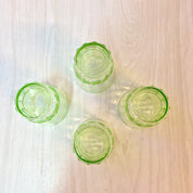 Green depression glass shot glasses with polka dot design, vintage barware vaseline glass set on wooden surface, overhead view