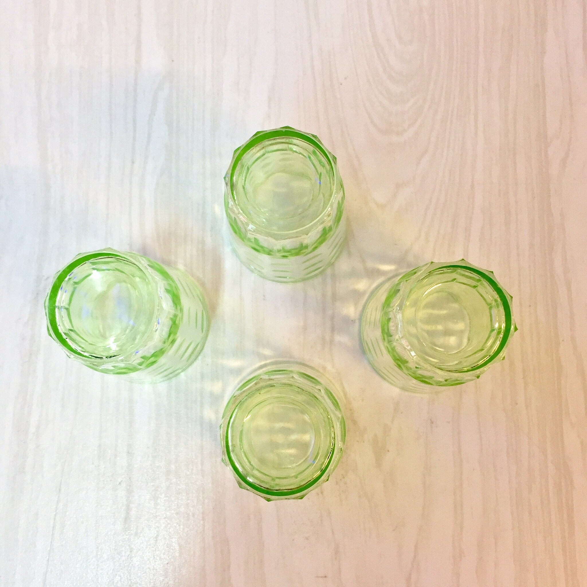 Green depression glass shot glasses with polka dot design, vintage barware vaseline glass set on wooden surface, overhead view