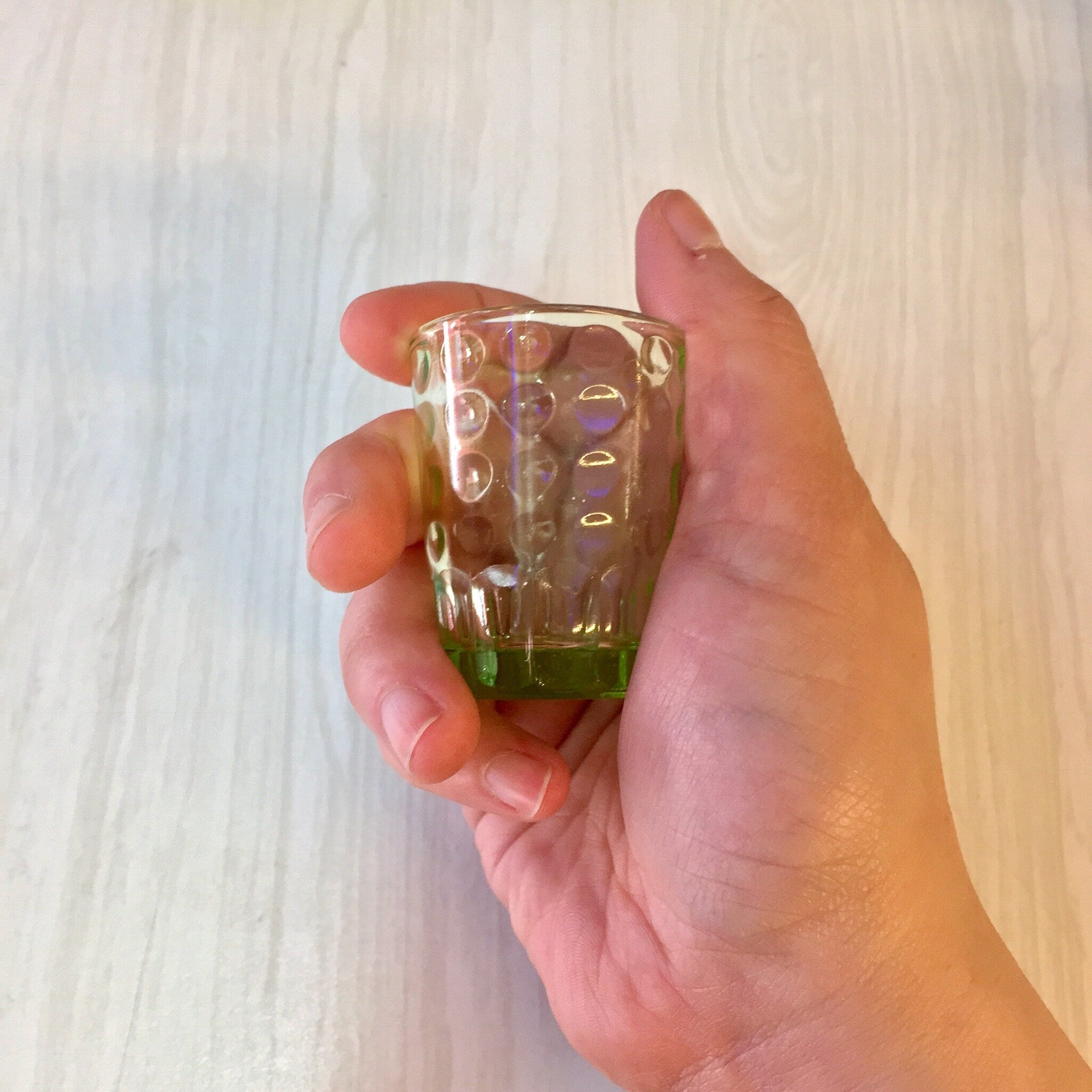 Vintage green Depression glass shot glass with polka dot design held in hand, showing translucent uranium glass known as Vaseline glass