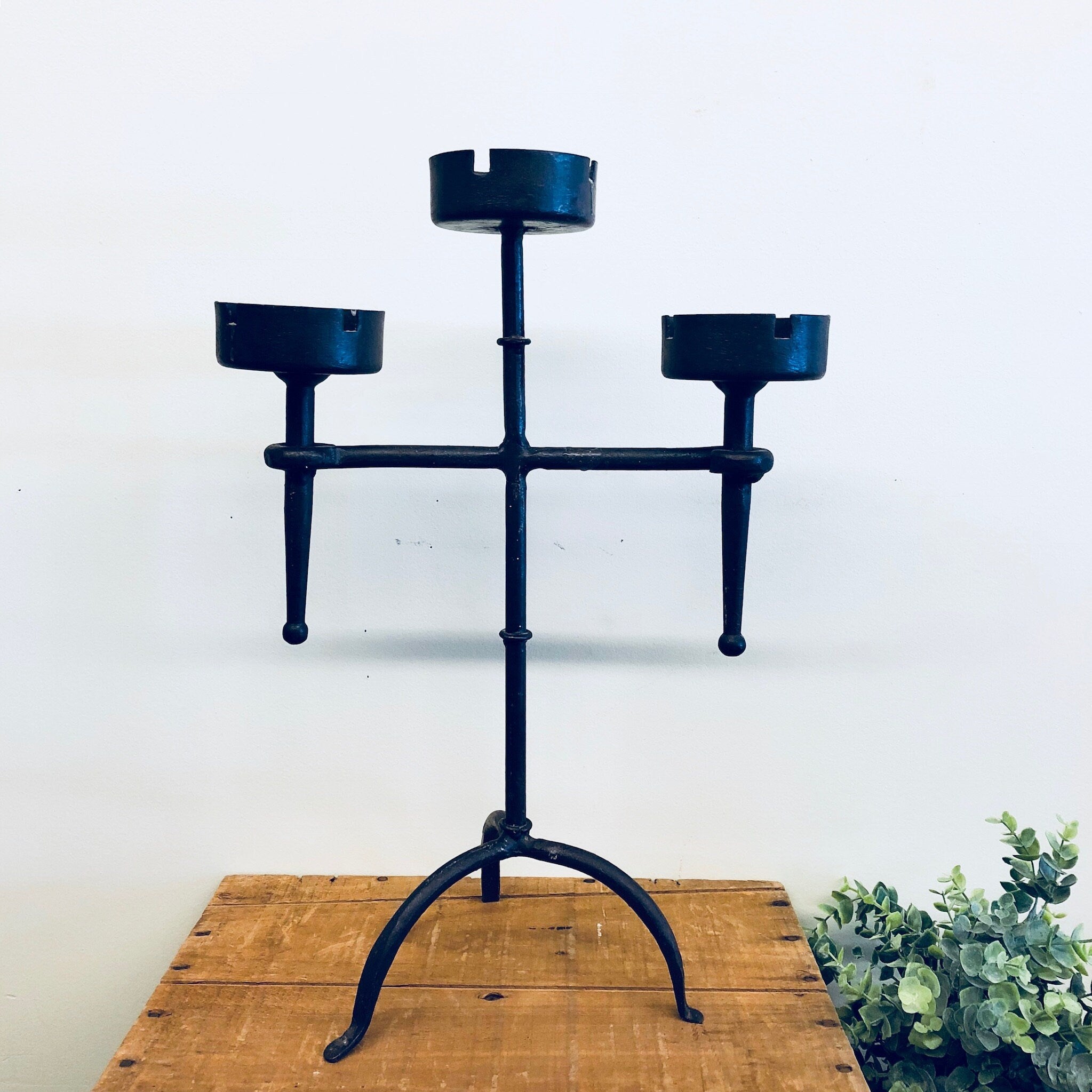 Vintage wrought iron candle holder with three arms on a wooden surface, suitable for use as a candlestick holder, ashtray, rustic home decor, mantle piece, or centerpiece.