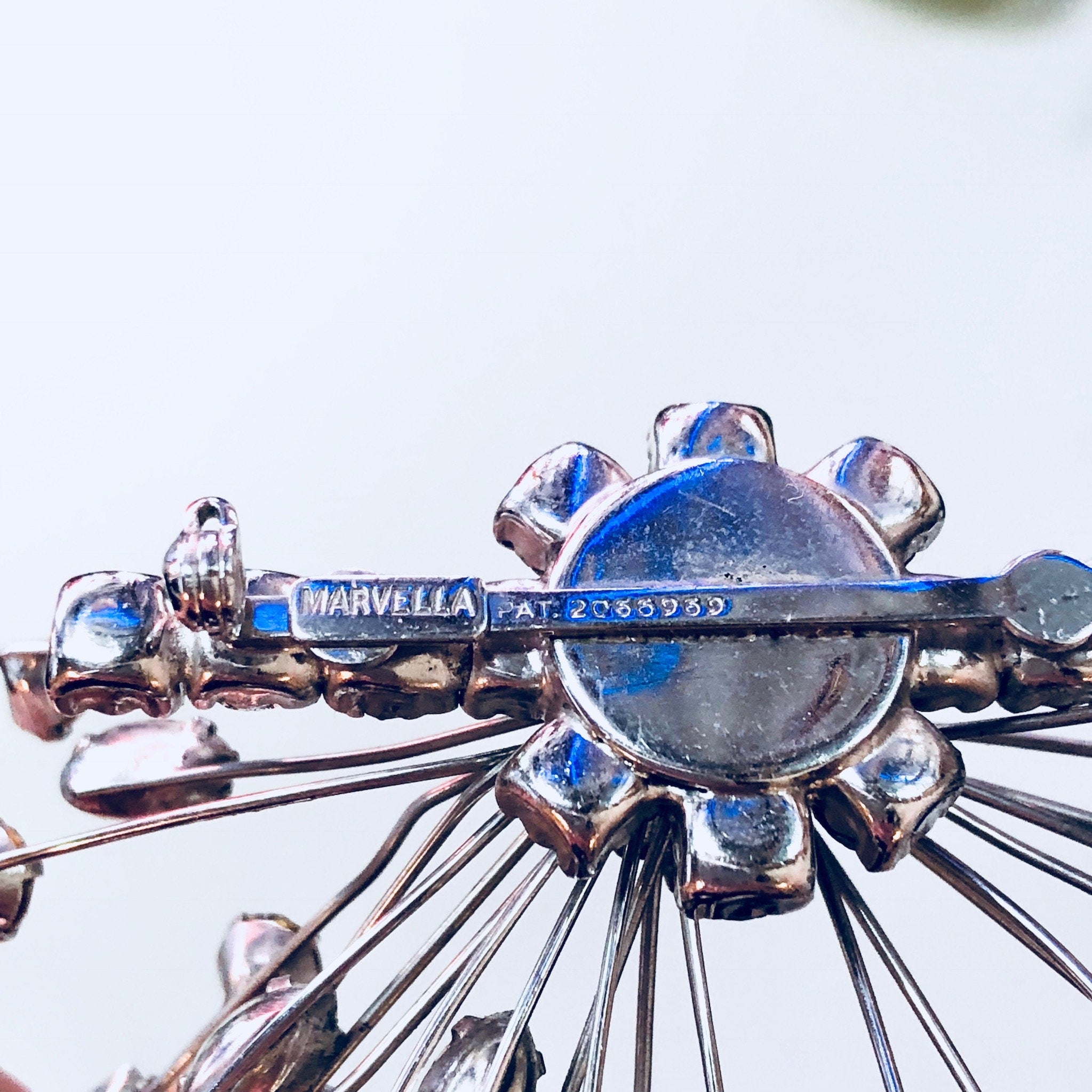 Close-up of a vintage Marvella jewelry set featuring a silver brooch with blue and clear rhinestones and matching clip-on earrings, showcasing an art deco design.