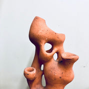 Terracotta sculpture resembling an abstract face with multiple hollow openings, suggesting a porous surface suitable for planting small herbs, succulents or strawberry plants, against a plain white background.