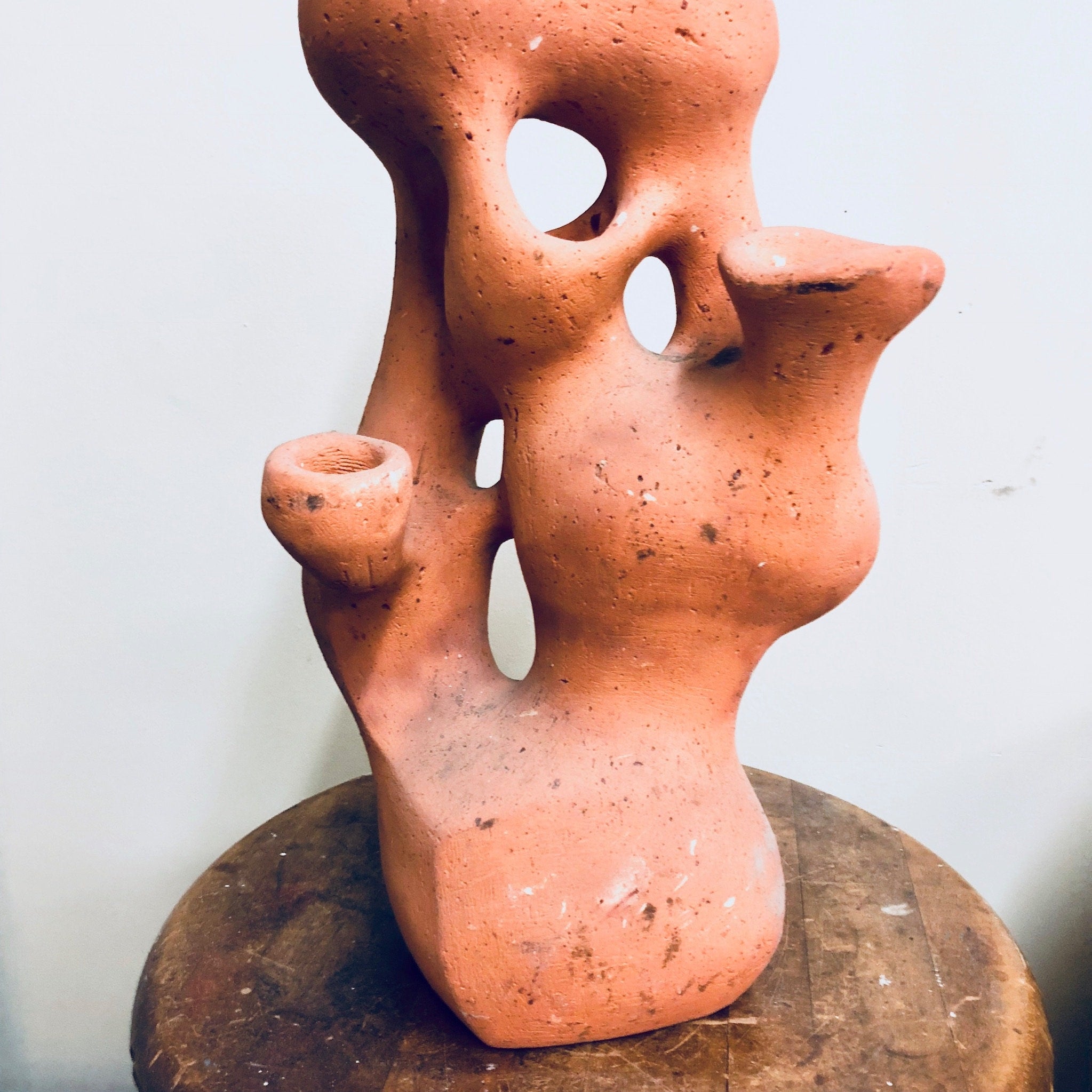 Terracotta abstract human-like sculpture with organic openings on a weathered surface, resembling an anthropomorphic planter or vessel for plants.