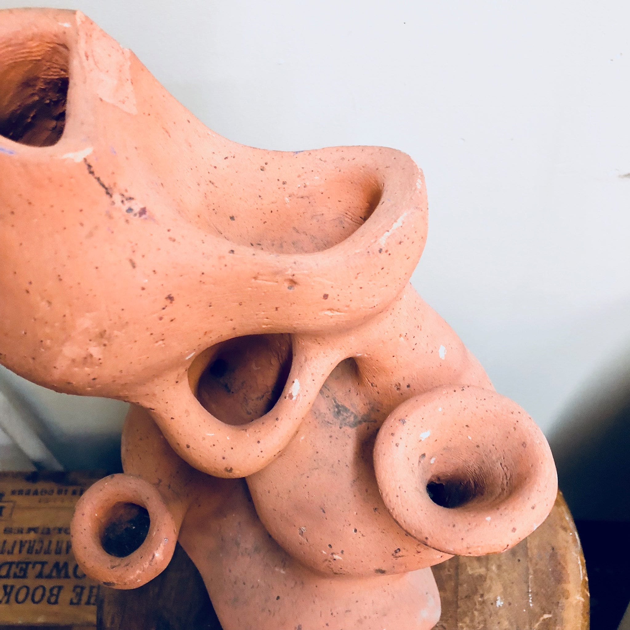 Terracotta planter with multiple holes in the shape of an abstract face, set against a blurred background.