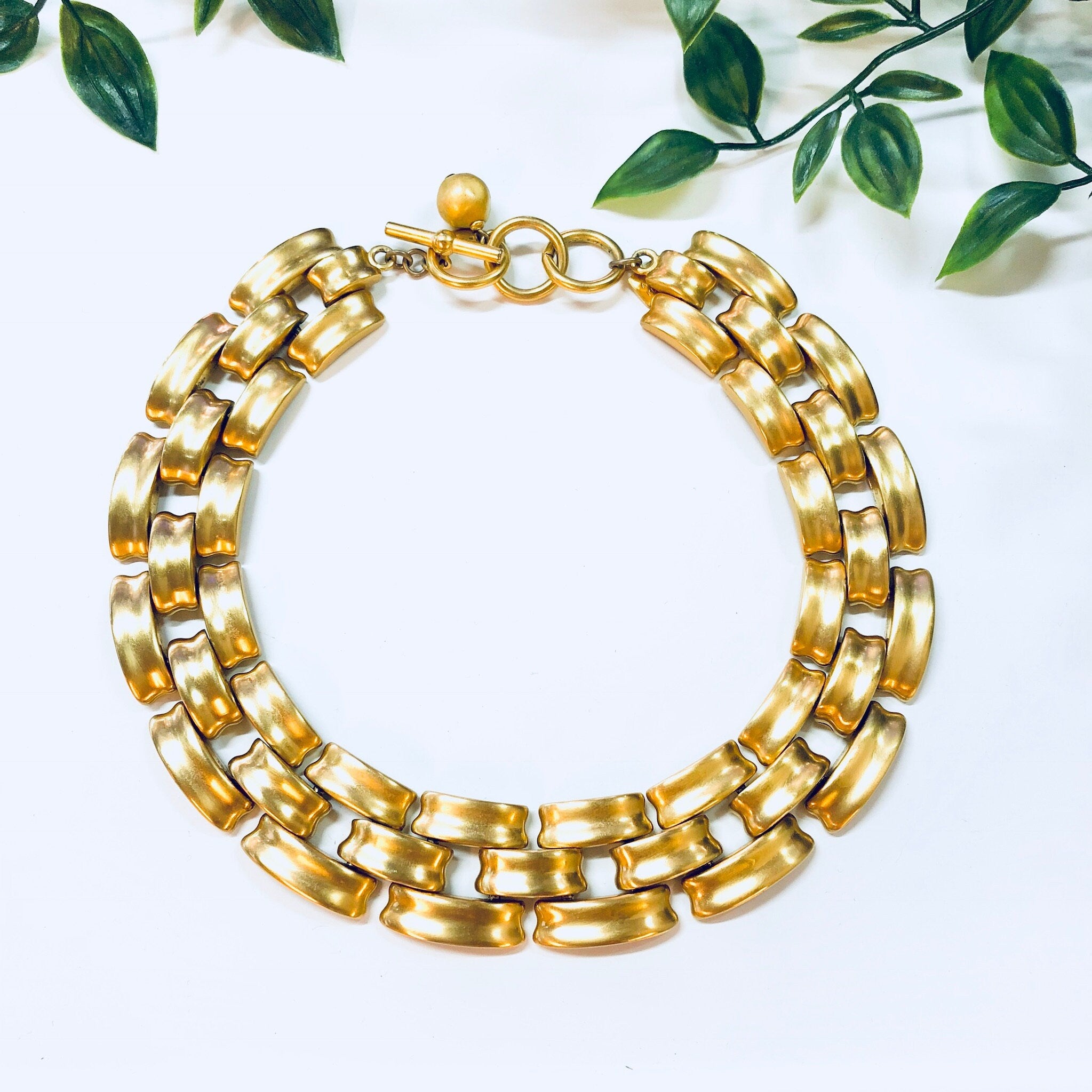 Vintage gold-toned chain link choker necklace by Anne Klein with toggle clasp, displayed on white background with greenery accents.