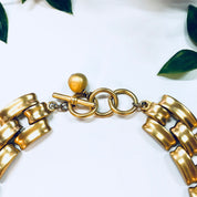 Vintage gold-toned Anne Klein chain link choker necklace with toggle closure, displayed on white background with green leaves.