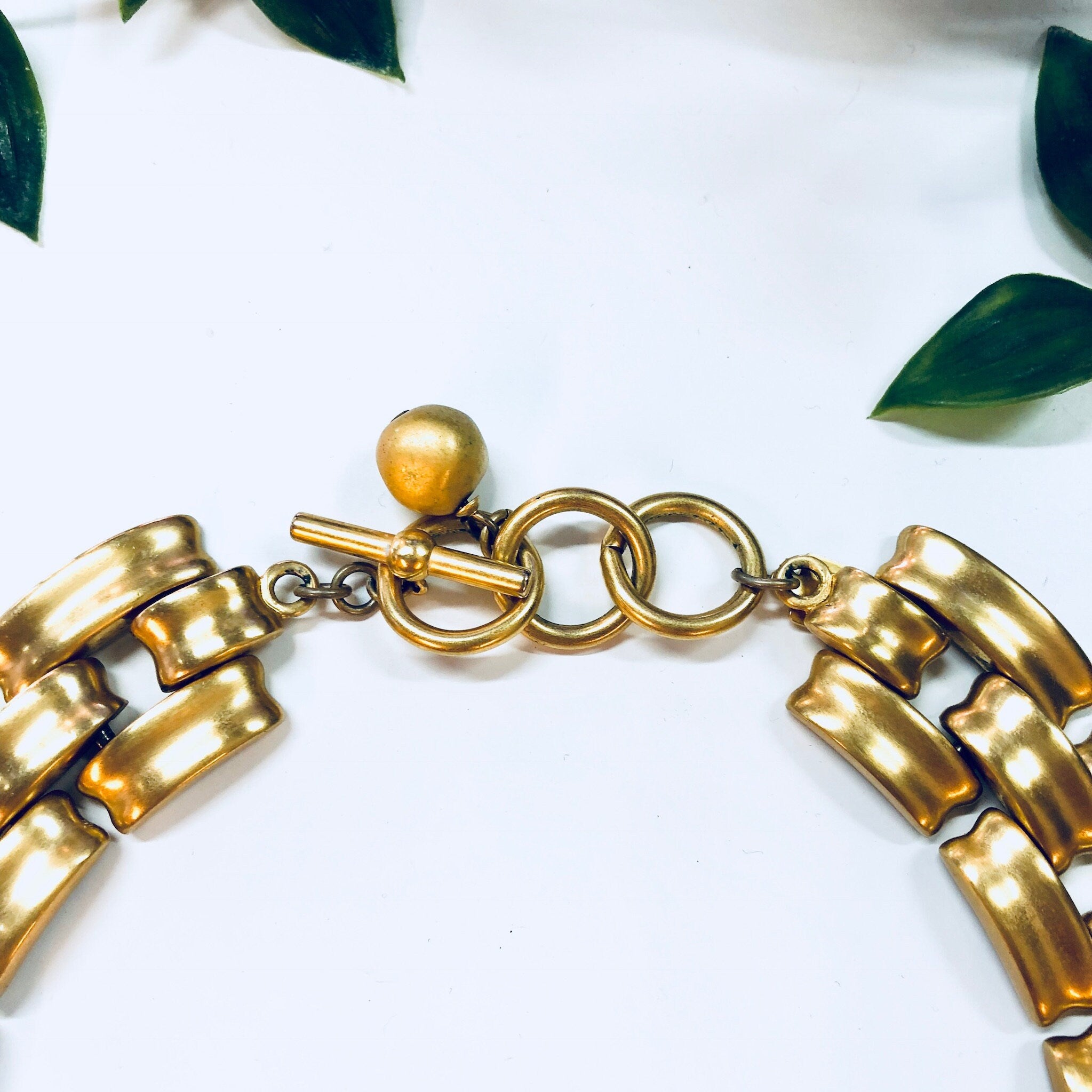 Vintage gold-toned Anne Klein chain link choker necklace with toggle closure, displayed on white background with green leaves.