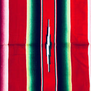 Colorful vintage Mexican blanket with stripes of red, blue, green, pink and yellow, featuring a central slit opening and fringe tassels at the edges, suitable as a throw blanket or for picnics.
