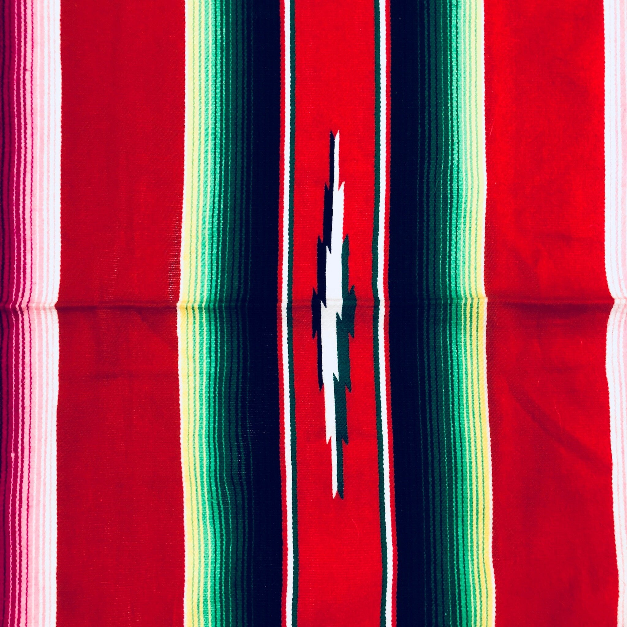 Colorful vintage Mexican blanket with stripes of red, blue, green, pink and yellow, featuring a central slit opening and fringe tassels at the edges, suitable as a throw blanket or for picnics.