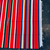Colorful vintage Mexican blanket with red, green, blue and white stripes on a dark background