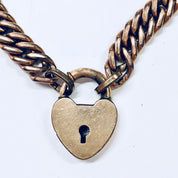 Vintage gold-toned chain bracelet with a heart-shaped locket charm, featuring a keyhole cutout design on the locket. The thick chain links have a braided pattern in blue enamel. Cute costume jewelry piece with a locked heart theme.