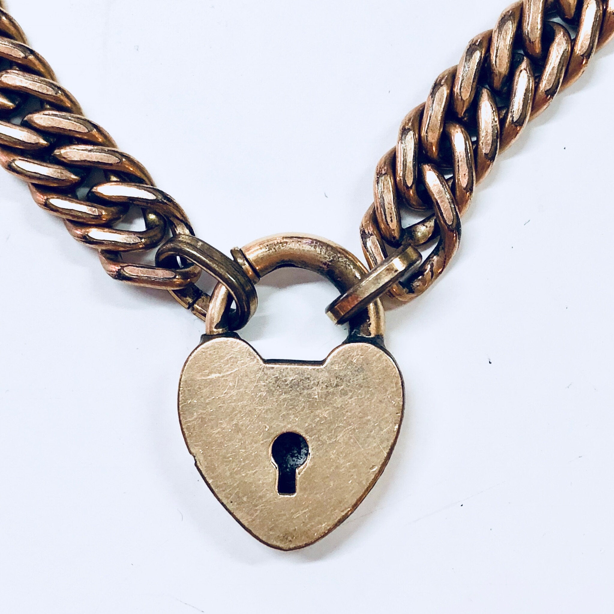 Vintage gold-toned chain bracelet with a heart-shaped locket charm, featuring a keyhole cutout design on the locket. The thick chain links have a braided pattern in blue enamel. Cute costume jewelry piece with a locked heart theme.