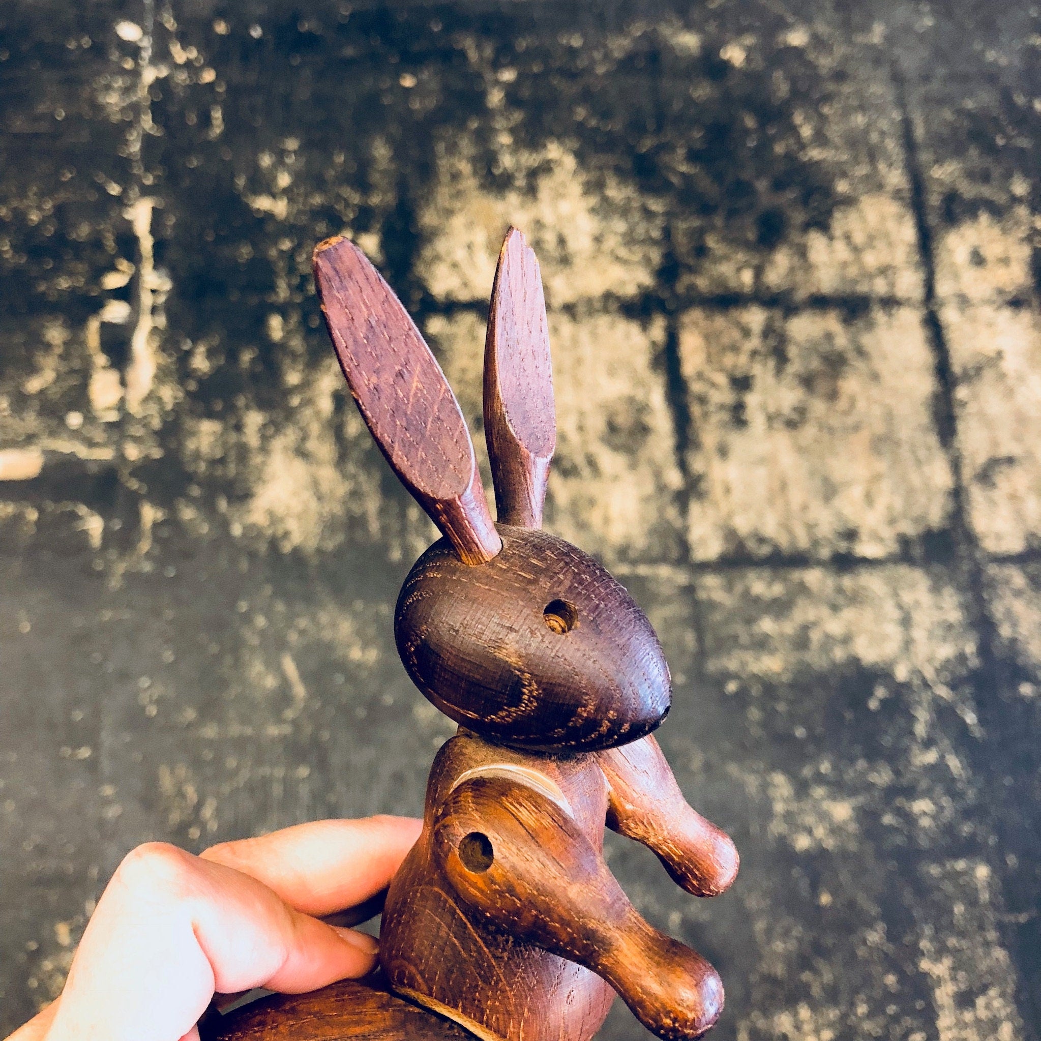 Wooden rabbit toy carving held in hand against grungy concrete background