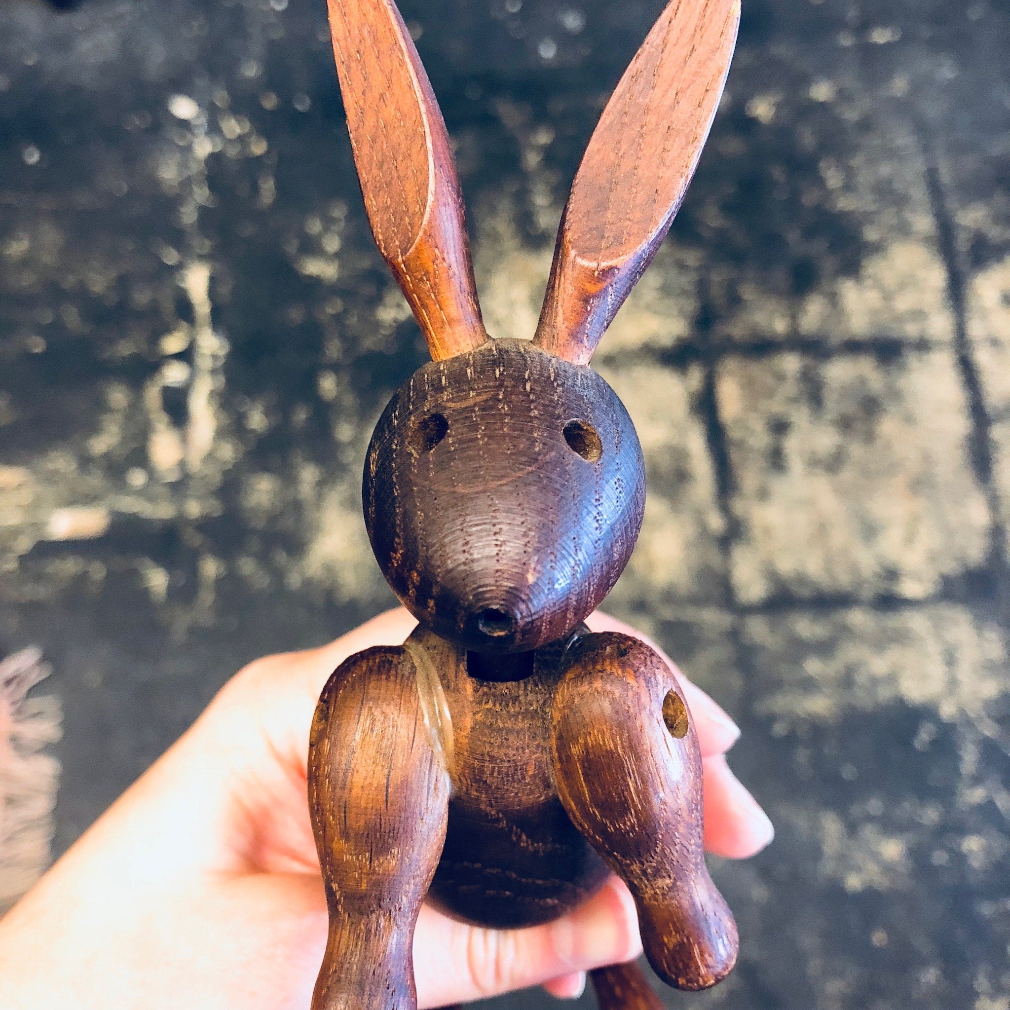 Hand holding a vintage carved wooden rabbit toy with large ears against a grungy textured background
