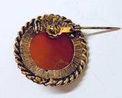 Vintage gold-toned round cameo brooch with intricate rope-like border design featuring an orange center stone