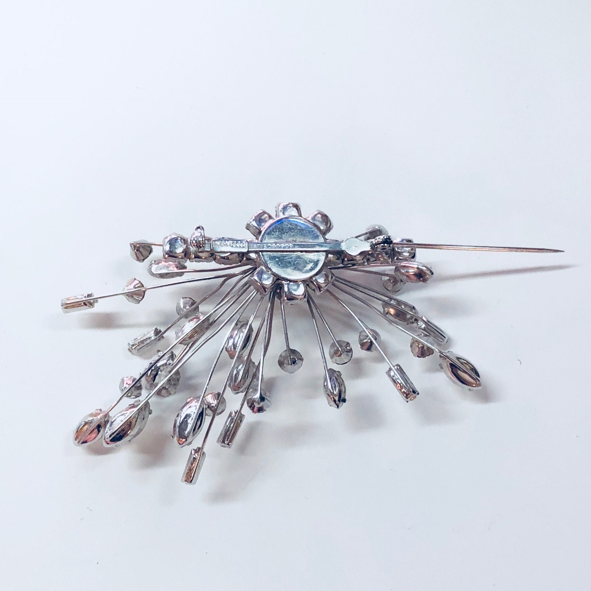 Silver Art Deco style Marvella brooch and clip-on earrings set with white rhinestones radiating out from a central blue stone, laying on a white background.