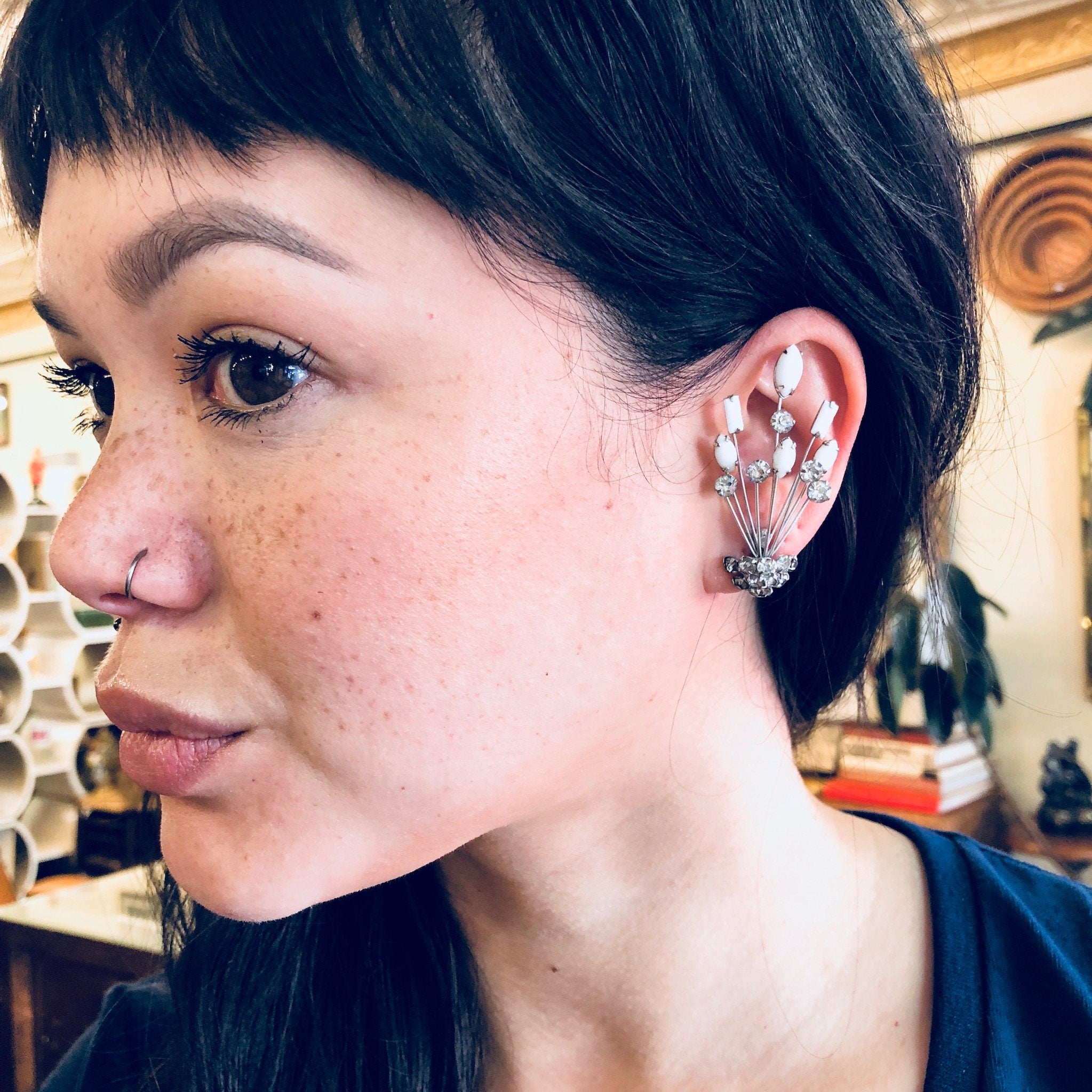 The image shows a close-up of a person with straight black hair wearing unique, silver-toned Art Deco style clip-on earrings shaped like fans or seashells, featuring white rhinestones. The earrings appear to be part of a Marvella jewelry set, likely including a matching brooch or pin.