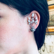 Close-up view of a woman's ear wearing an ornate silver earring with dangling rhinestones and white stones, designed in an Art Deco style by Marvella jewelry.