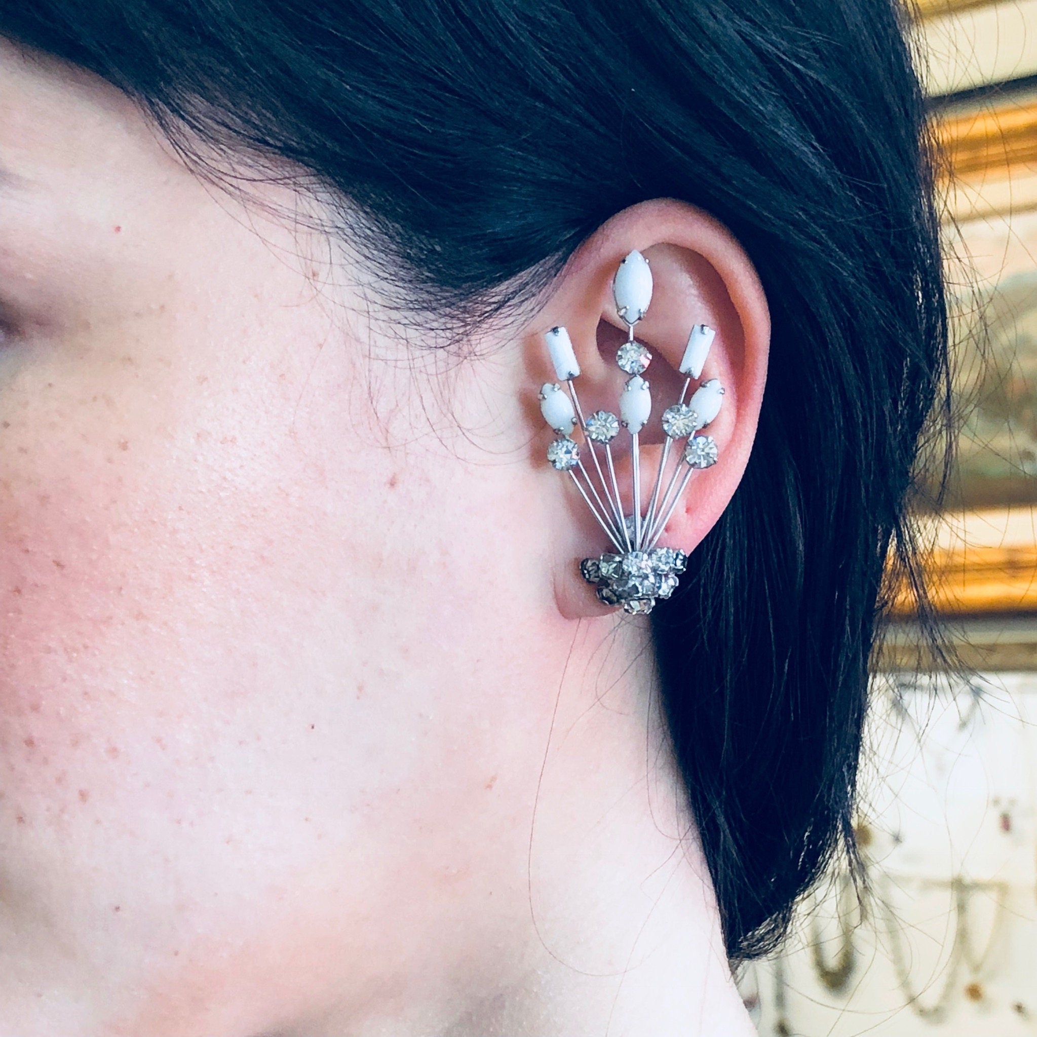 Close-up view of a woman's ear wearing an ornate silver earring with dangling rhinestones and white stones, designed in an Art Deco style by Marvella jewelry.