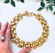 Vintage gold-toned Anne Klein thick chain link choker necklace with toggle clasp, held in hand above white background with green leaves