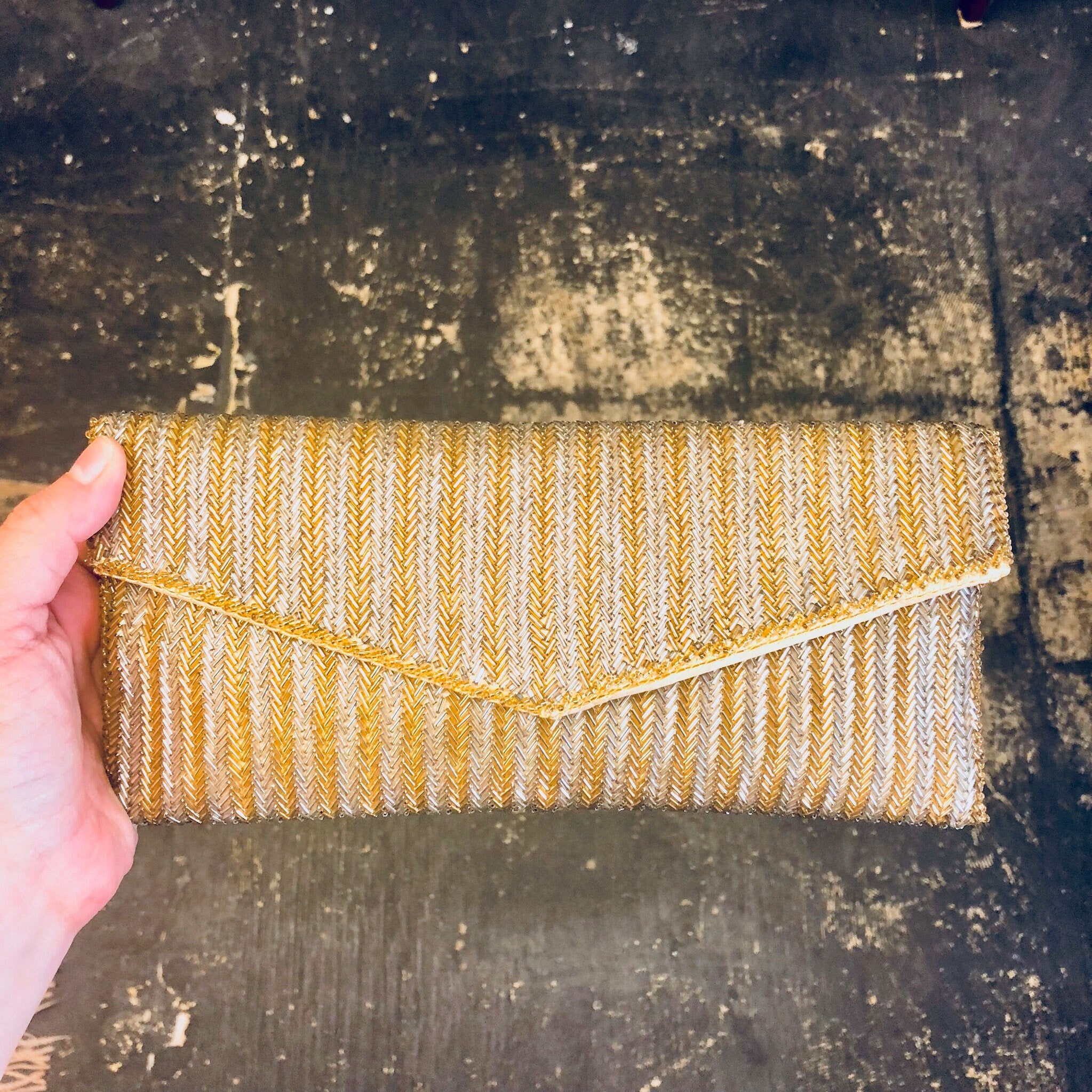 Vintage yellow beaded envelope clutch purse with gold and silver beads, suitable for formalwear, weddings and special occasions, held in hand against distressed dark background.