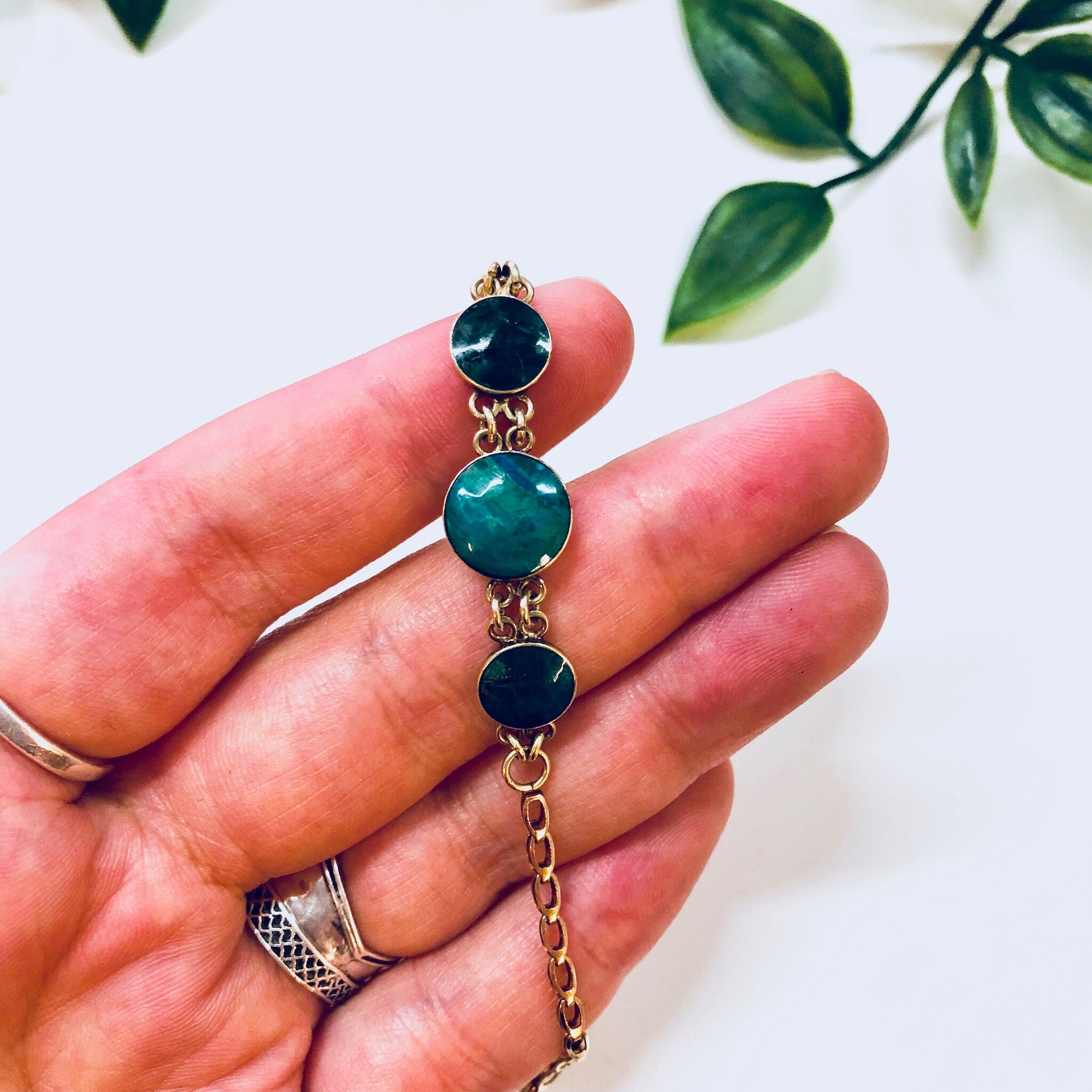 Vintage 14K gold link bracelet with deep blue and iridescent green natural stone beads, held in a person's hand against a white background with greenery.