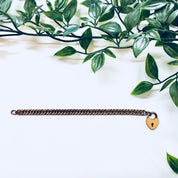 Vintage gold-toned heart locket bracelet with thick chain, resting on white surface with green foliage in the background.