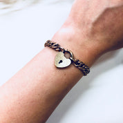 Vintage heart locket bracelet with thick gold-toned chain, worn on wrist. Unique costume jewelry piece with locked heart charm.