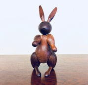 Vintage wooden rabbit toy carving with movable arms and legs, handcrafted from rich brown wood with a spherical head, standing on a reflective wooden surface.