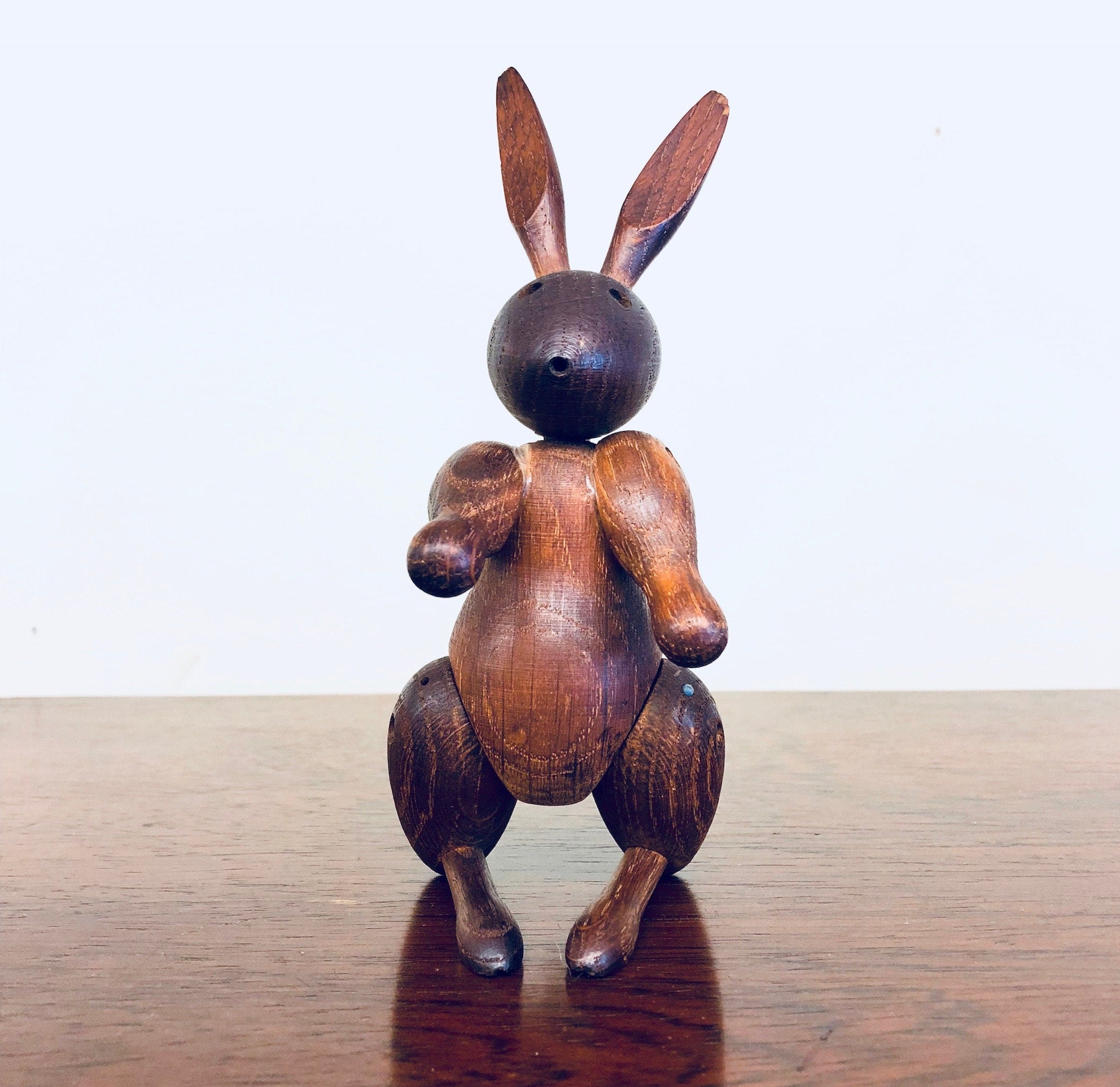 Vintage wooden rabbit toy carving with movable arms and legs, handcrafted from rich brown wood with a spherical head, standing on a reflective wooden surface.