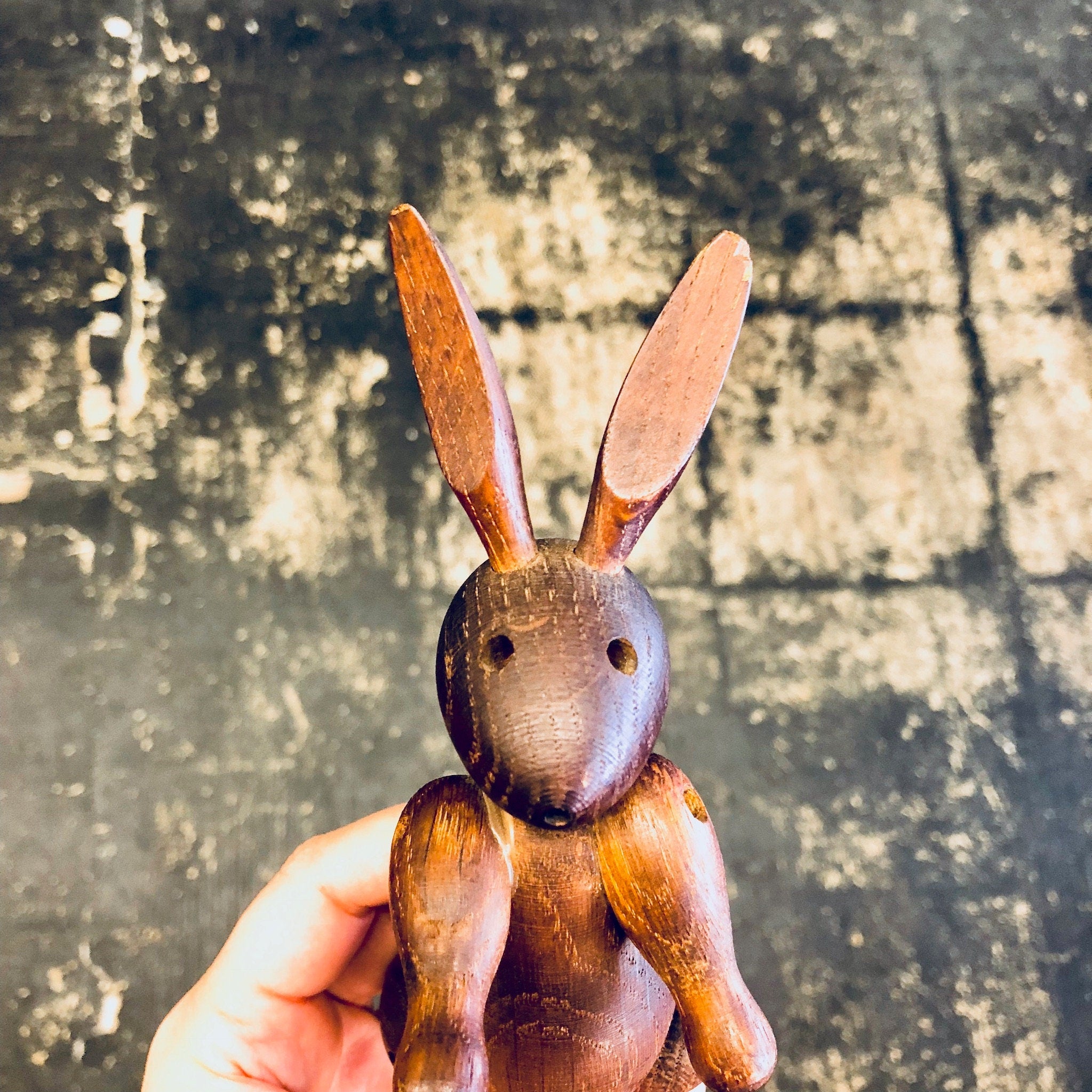 Wooden carved rabbit toy held in hand against rustic textured background