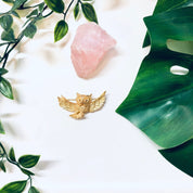 Vintage gold-toned owl brooch by Trifari displayed on white fabric with pink quartz crystal and green leaves.