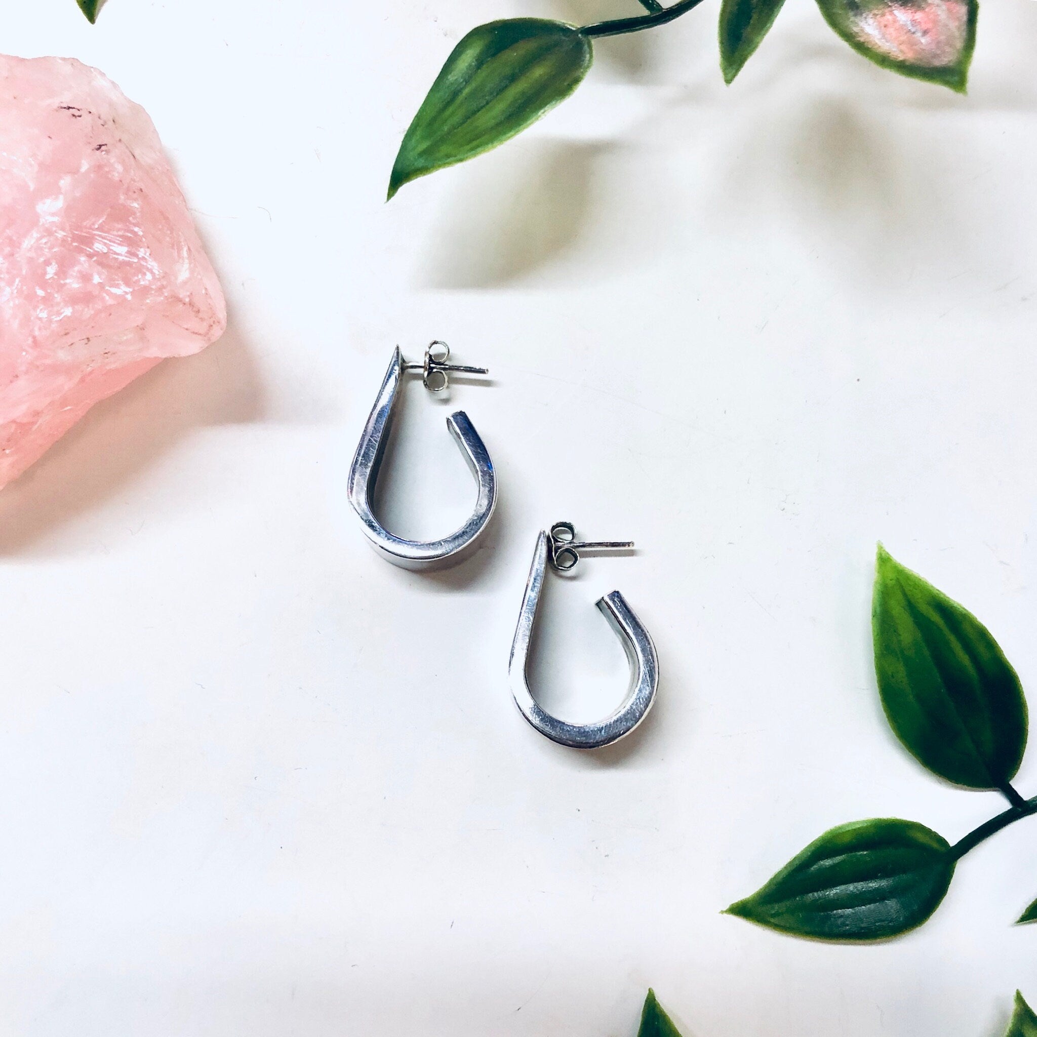 Vintage silver teardrop earrings by ZINA surrounded by green leaves on a white background