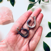 Vintage silver modernist teardrop earrings by Zina held in palm with green leaves in background