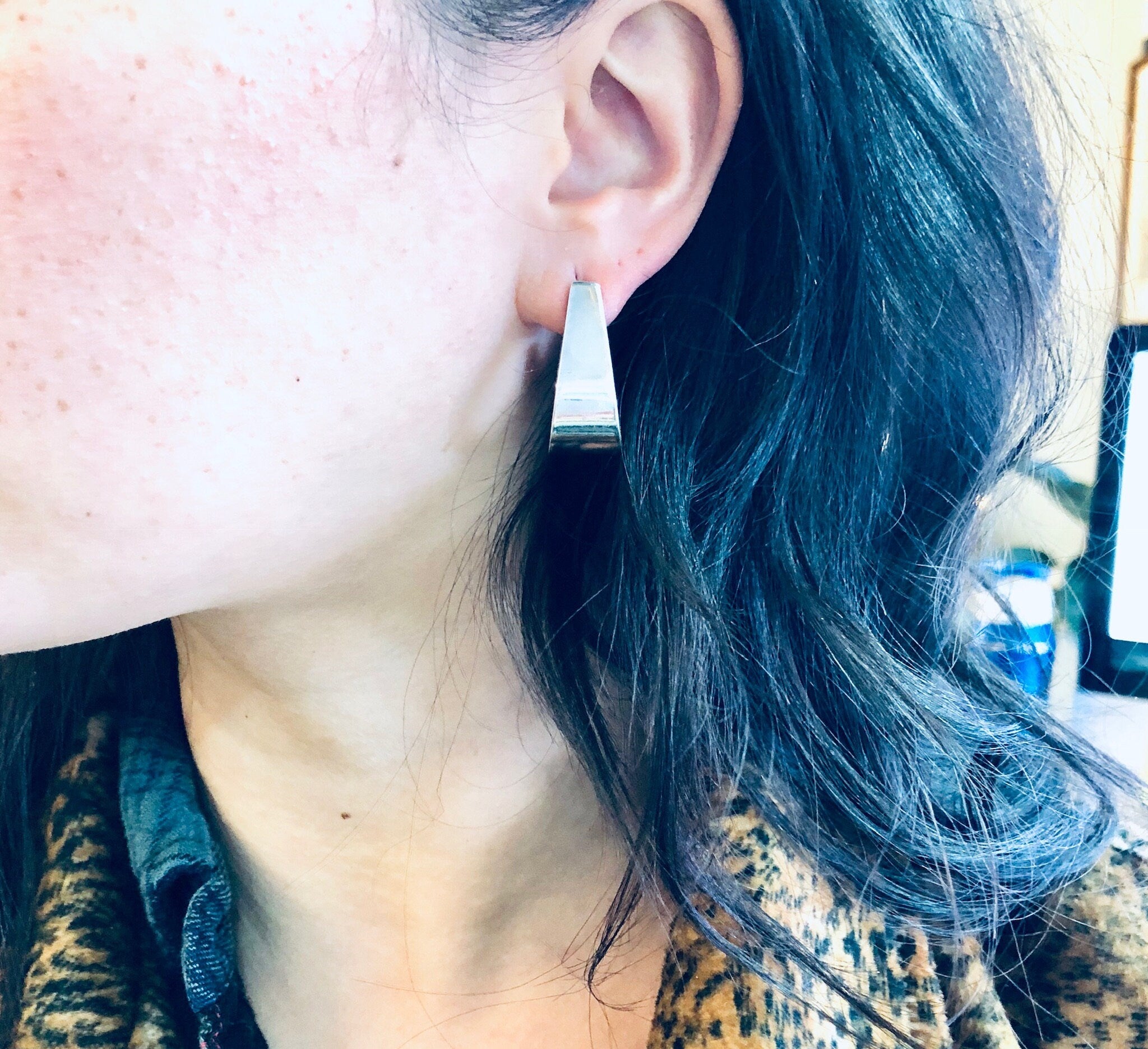 Close-up view of a woman wearing vintage modernist thick sterling silver Zina earrings, with long blue hair obscuring part of her face.