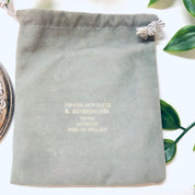 Vintage sterling silver compact mirror from Towle Silversmiths, with drawstring pouch and engraving "Wayne Ashmore King of Prussia". The mirror is shown on a white surface surrounded by green leaves.