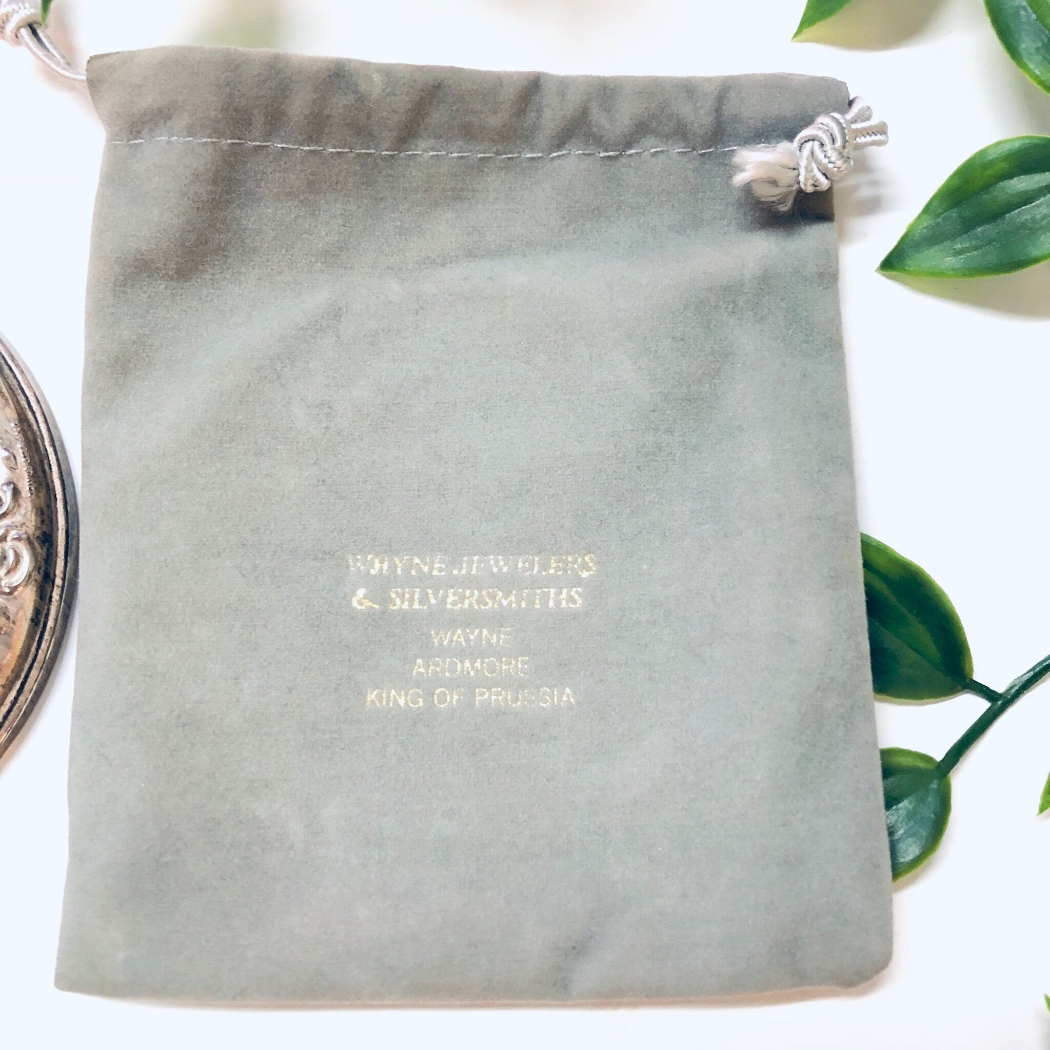 Vintage sterling silver compact mirror from Towle Silversmiths, with drawstring pouch and engraving "Wayne Ashmore King of Prussia". The mirror is shown on a white surface surrounded by green leaves.